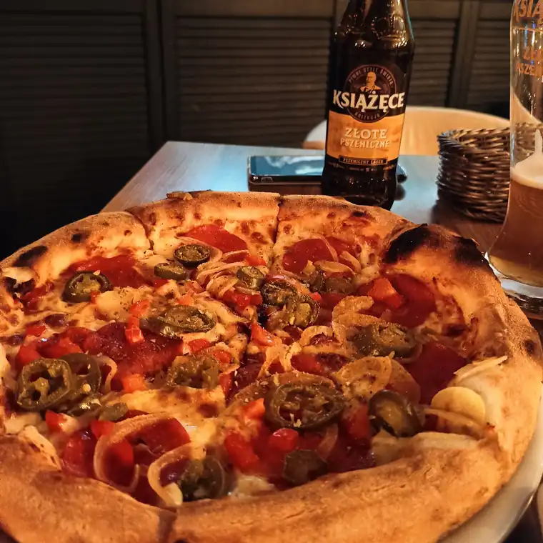 Pizza z salami i jalapeño na stole w Pizzerii EMI, w tle butelka piwa i podświetlone akwarium
