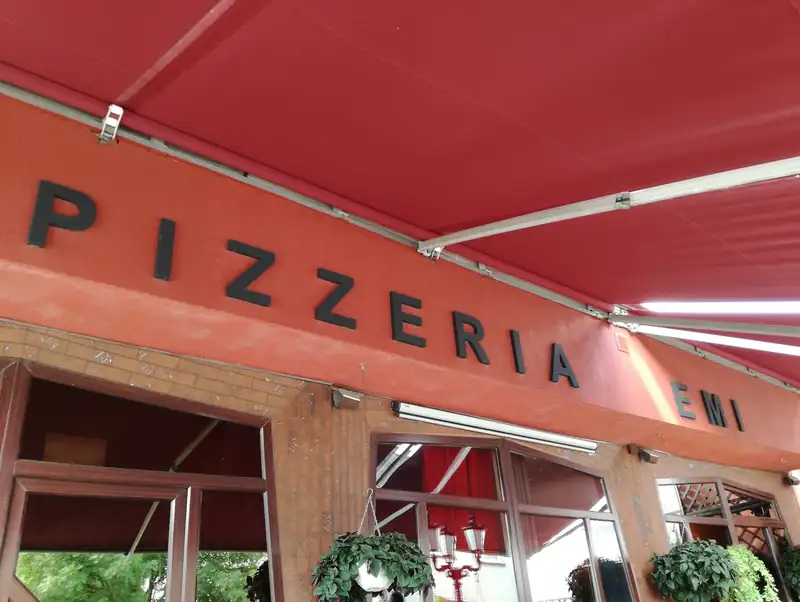 Czerwona markiza z białym napisem PIZZERIA nad wejściem i oknami