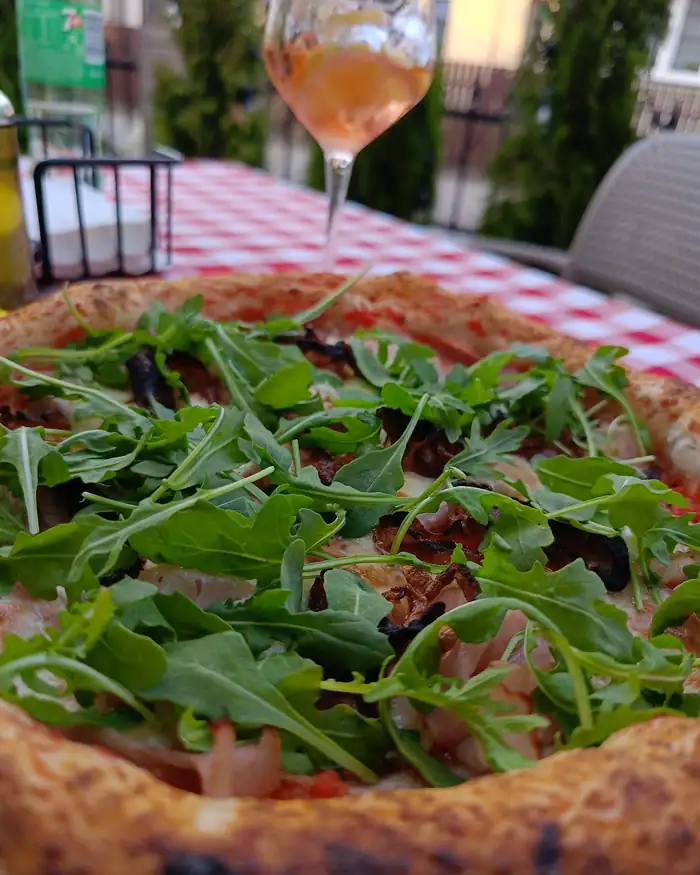 Pizza z rukolą i pomidorkami koktajlowymi na stole z kieliszkiem wina