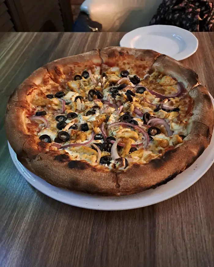 Pizza z szynką, czerwoną cebulą i oliwkami na drewnianym stole
