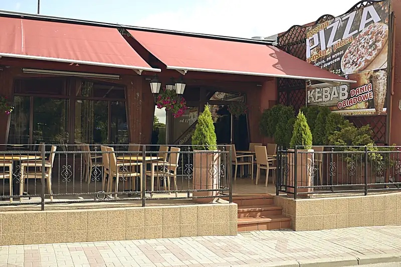 Taras z krzesłami pod czerwoną markizą i szyld Pizza Kebab